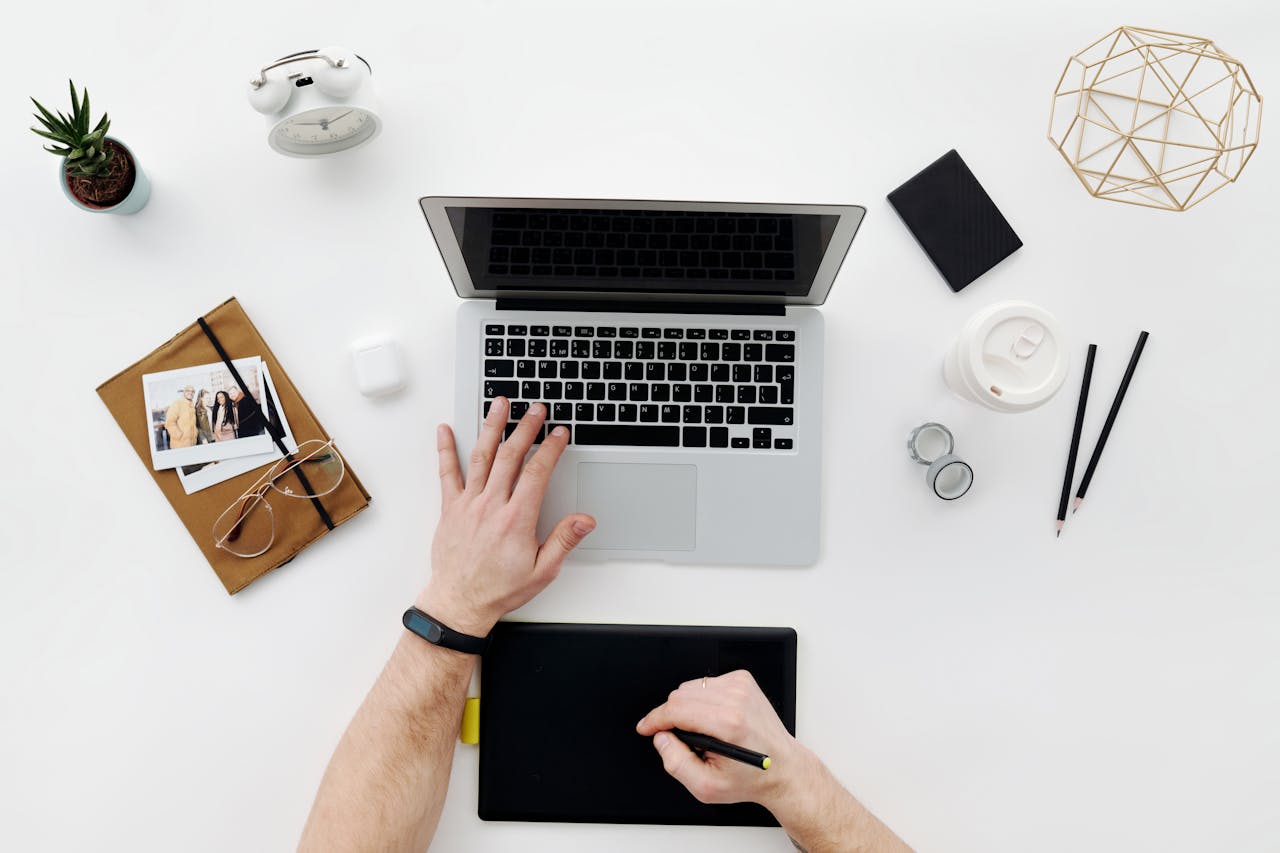 Modern workspace featuring a laptop, drawing tablet, and office essentials from above.
