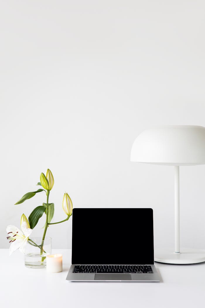 A modern minimalist workspace featuring a laptop, white lamp, and fresh flowers on a desk.